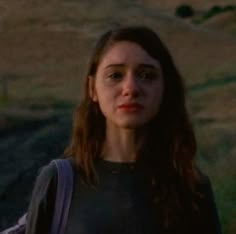 a woman with long hair standing in front of a field and looking at the camera