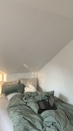 an unmade bed in the corner of a room with white walls and slanted ceilings