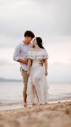 a man and woman standing on the beach next to each other with their arms around each other