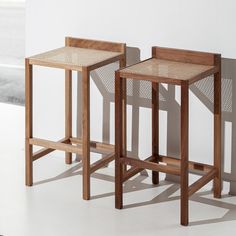 two wooden stools sitting next to each other in front of a white wall and window