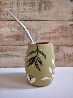 a toothbrush holder with an olive branch painted on the front and bottom, sitting on a white surface