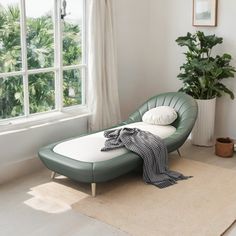 a green chaise lounger sitting in front of a window next to a potted plant