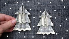 two origami christmas trees made out of dollar bills are being held by someone's hand