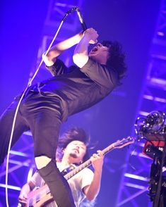 two men on stage with microphones and guitar in the foreground, one singing