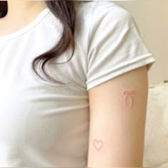 a woman wearing a white t - shirt with a pink heart tattoo on her arm