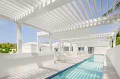 an outdoor swimming pool with white pergolated roofing and blue skies in the background