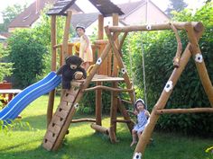 two children are playing on a wooden swing set in the yard with their teddy bear