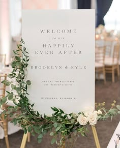 a welcome sign with greenery and white flowers on it at a wedding reception in brooklyn, new york