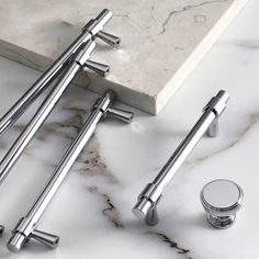 four chrome handles on a marble countertop next to two silver knobs and an empty glass container