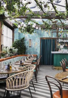 an outdoor dining area with tables, chairs and potted plants on the wall behind it