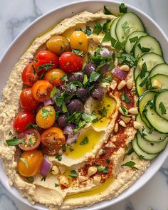 a bowl filled with hummus, olives, tomatoes and cucumbers