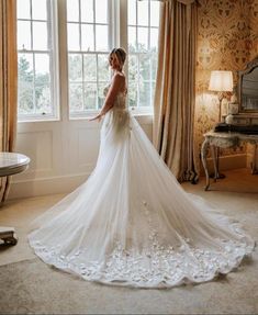 a woman standing in front of a window wearing a wedding dress