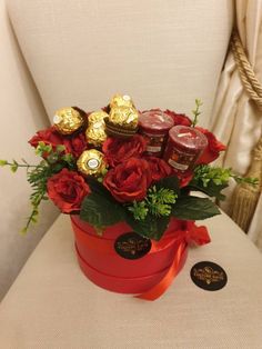 a bouquet of roses and chocolates in a red box on a white chair with a gold sticker