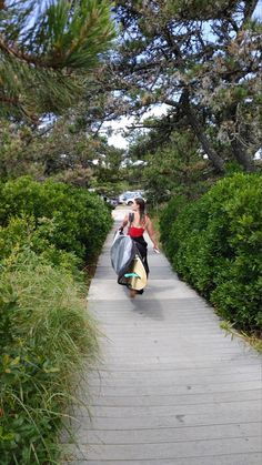 a woman walking down a sidewalk carrying shopping bags and a surfboard in her hand