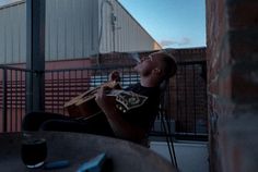 a man sitting on top of a metal table next to a building holding a guitar