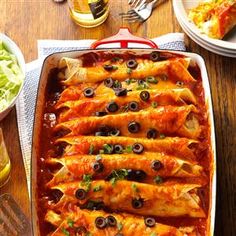 an enchilada dish with olives and meat in it on a wooden table