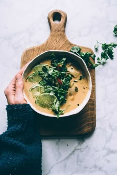 a person holding a bowl of soup on top of a cutting board