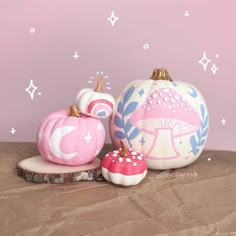 three painted pumpkins sitting next to each other on a piece of wood in front of a pink wall