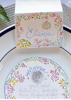 a white plate topped with a box filled with writing next to a green leafy plant