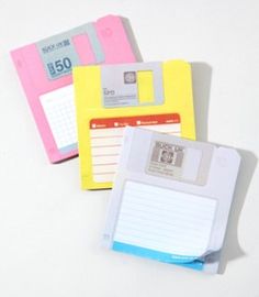 three different colored floppy disks with notepads attached to each one, on a white surface