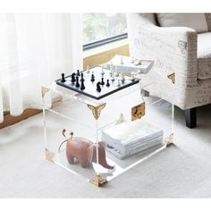 a glass coffee table with chess pieces on it in front of a chair and window