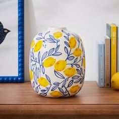 a yellow and blue vase sitting on top of a wooden table next to bookshelves