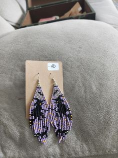 purple and black seed beaded earrings with white beads on the end, sitting on a couch