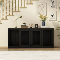 a living room with stairs and pictures on the wall next to a black sideboard