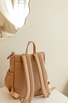 a tan purse sitting on top of a white table next to a mirror with a reflection in it