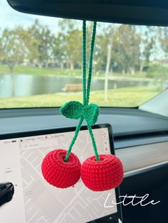 two crocheted cherries hanging from the dashboard of a car in front of a computer