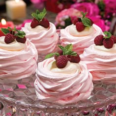 several small desserts on a glass plate with raspberries and cream frosting