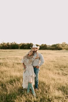 a man and woman are standing in the middle of a field with tall grass, wearing cowboy hats