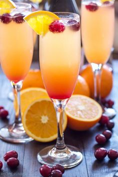 two glasses filled with orange juice and garnished with cranberries on a wooden table