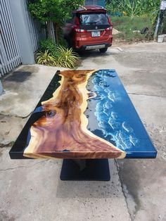 a table made out of wood and glass sitting on the side of a road next to a red car