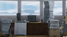 an office filled with stacks of papers next to a large window and a computer desk