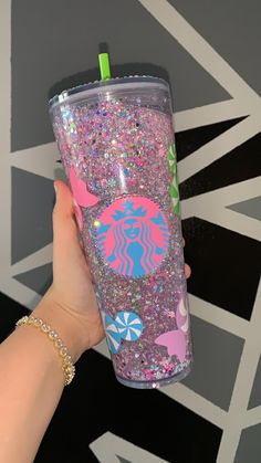 a person holding up a starbucks cup with glitter on the bottom and pink, blue, green, and white designs