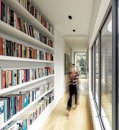 a woman walking down a hallway next to a bookshelf filled with lots of books