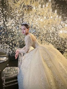 a woman in a wedding dress sitting at a table with a chandelier behind her