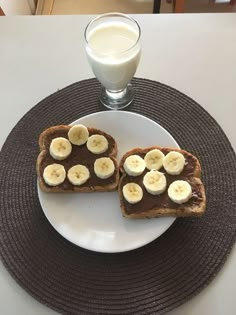 two pieces of toast with banana slices and chocolate spread on top, sitting on a plate next to a glass of milk