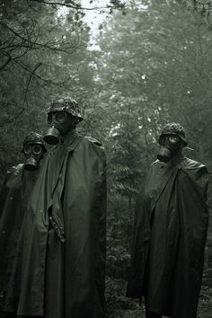 three people wearing gas masks and raincoats standing in the middle of a forest