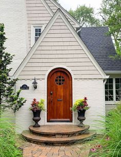 a white house with a wooden door and two planters on the front steps next to it