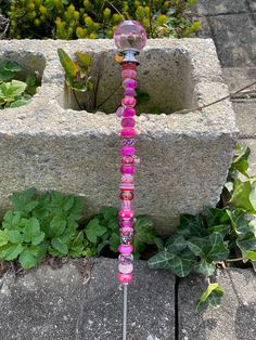 a pink and purple glass beaded stick sitting on top of a cement block next to plants