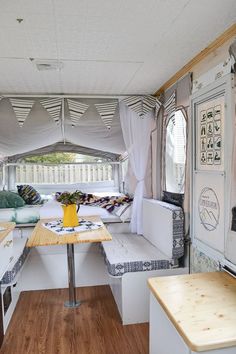 the inside of a camper with wood flooring and white curtains on the windows