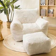 a white chair and ottoman in a living room with potted plants on the floor