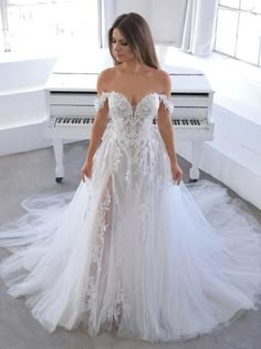 a woman standing in front of a piano wearing a white gown with sheer lace and flowers