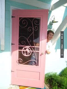 a woman standing in front of a pink door with an iron design on it's side