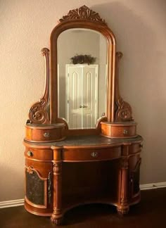 an ornate wooden vanity with mirror and drawers in front of a white door on the wall