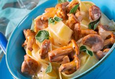 a blue bowl filled with pasta and meat covered in sauce, cheese and spinach