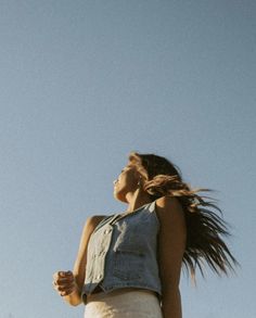 a woman with her hair blowing in the wind, looking up into the blue sky