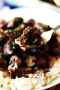 a white plate topped with rice and meat covered in gravy on top of a wooden table